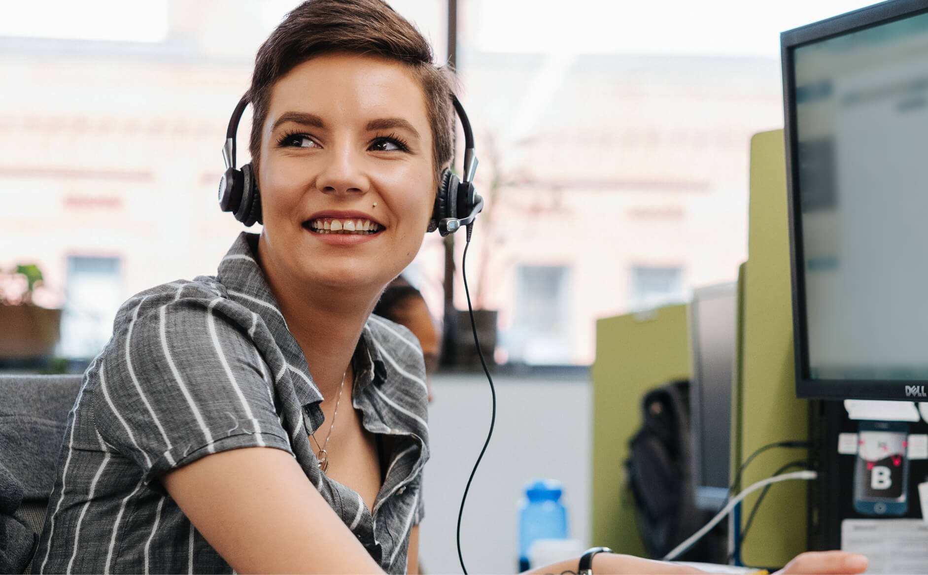 Capital One customer care associate sits at computer and turns and smiles with headset on